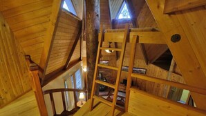 Un intérieur en bois avec un escalier menant à une mezzanine, agrémentée de poutres en bois et d’une échelle.