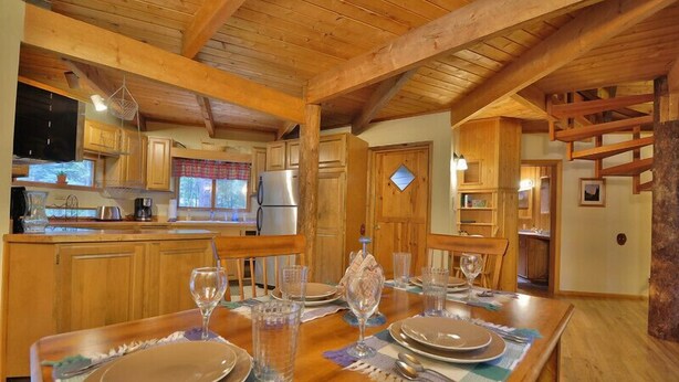 Un intérieur en bois comprenant une table à manger pour quatre personnes, un coin cuisine avec des placards en bois et une cheminée en pierre.