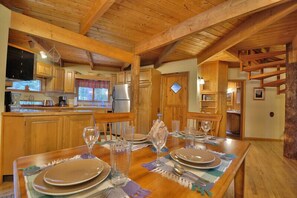 A wooden interior with a dining table set for four, a kitchen area with wooden cabinets, and a stone fireplace. - Custom Home in a Great Location with Outdoor Hot Tub (Hungry Horse)