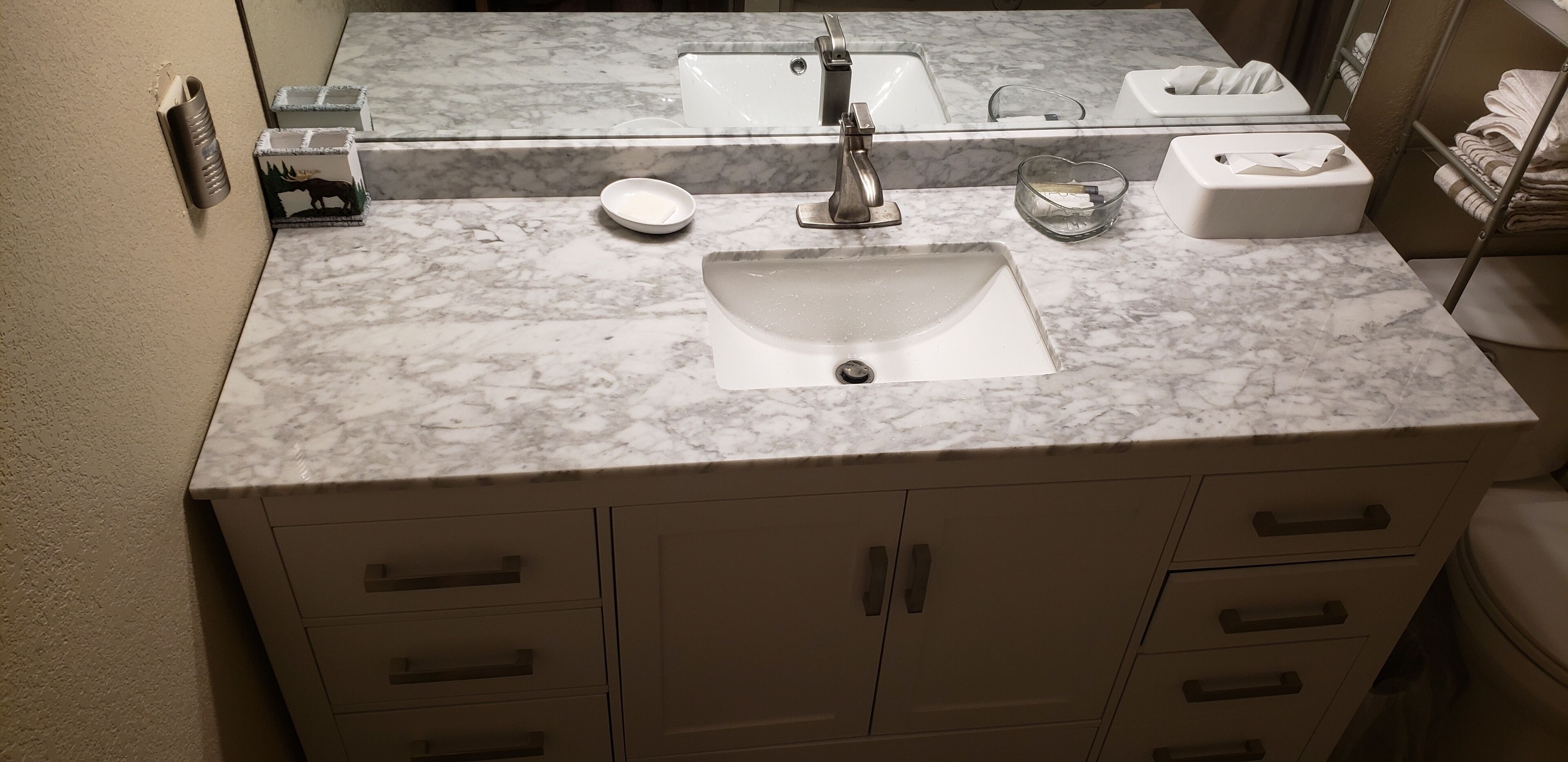 Un baño con lavamanos de mármol, espejo y toallero.