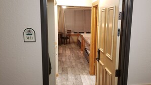 A narrow hallway with a wooden floor, a door on the right, and a window with blinds in the background. - Brian head Studio in 3.5 star Cedar Breaks Lodge - Sleeps 4 (Brian Head)