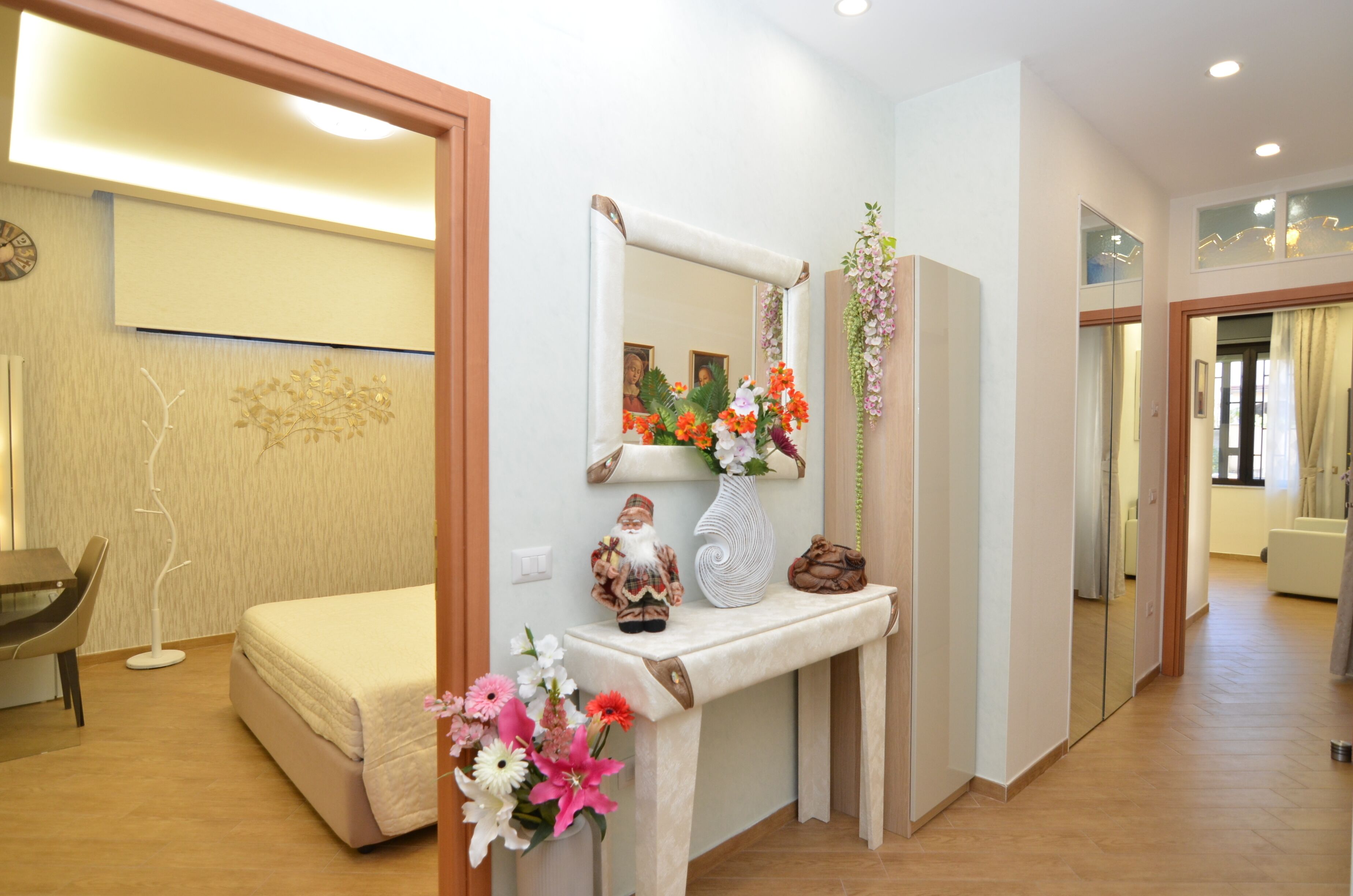 Habitación de hotel con cama, mesita de noche, espejo y un jarrón decorativo con flores.