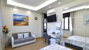 Habitación de hotel con sofá, escritorio, cama, televisor y un cuadro en la pared.