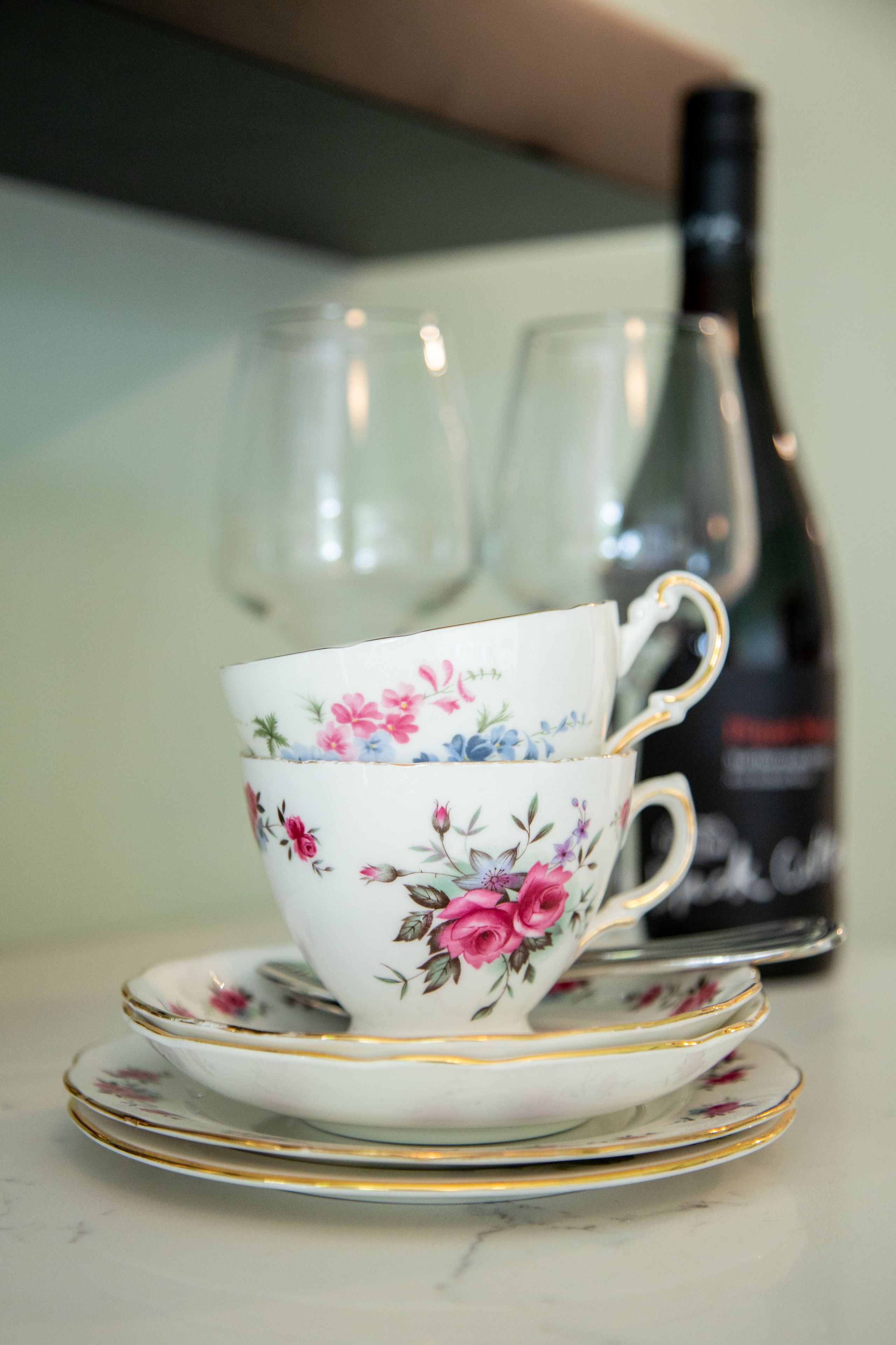 A floral-patterned cup and saucer on a table with a bottle in the background.