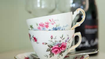 A floral-patterned cup and saucer on a table with a bottle in the background.