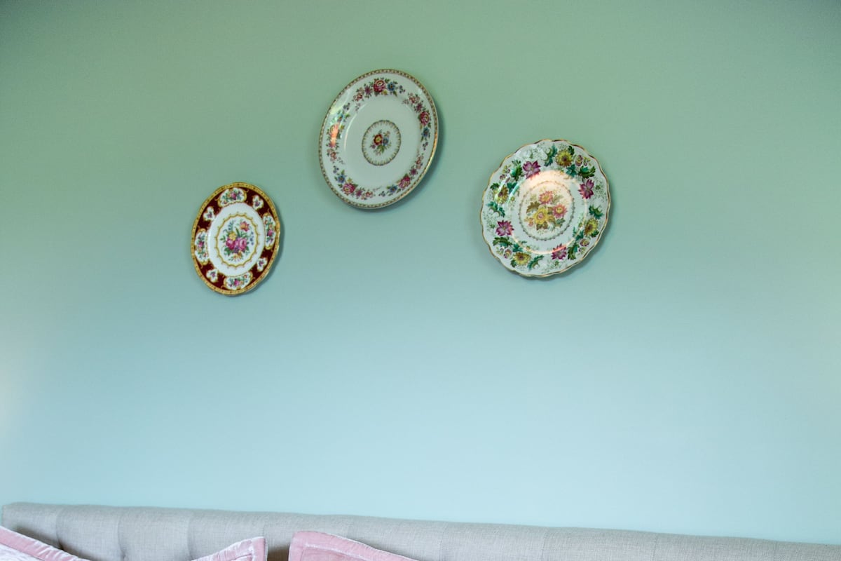 A bed with floral bedding and three decorative plates on the wall.