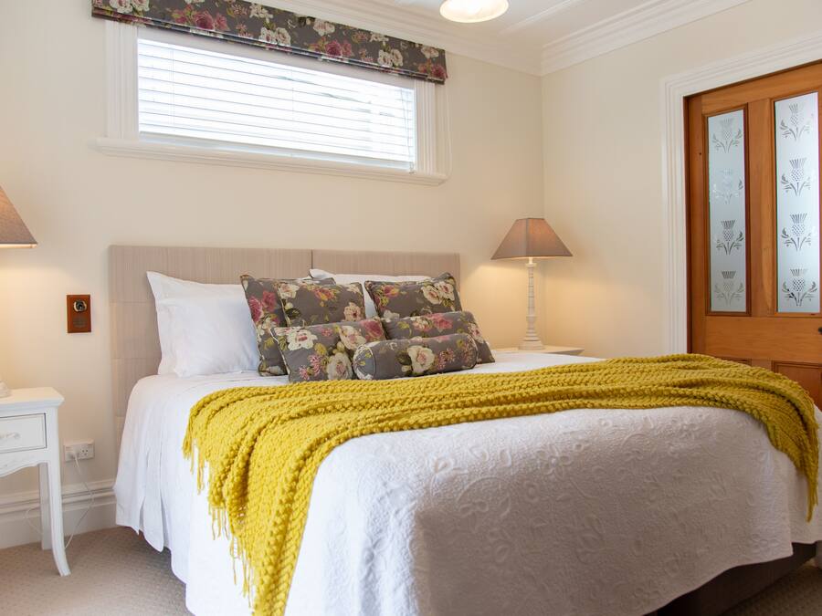 Una cama bien hecha con una manta amarilla, dos lámparas de noche y un cabecero estampado con flores.