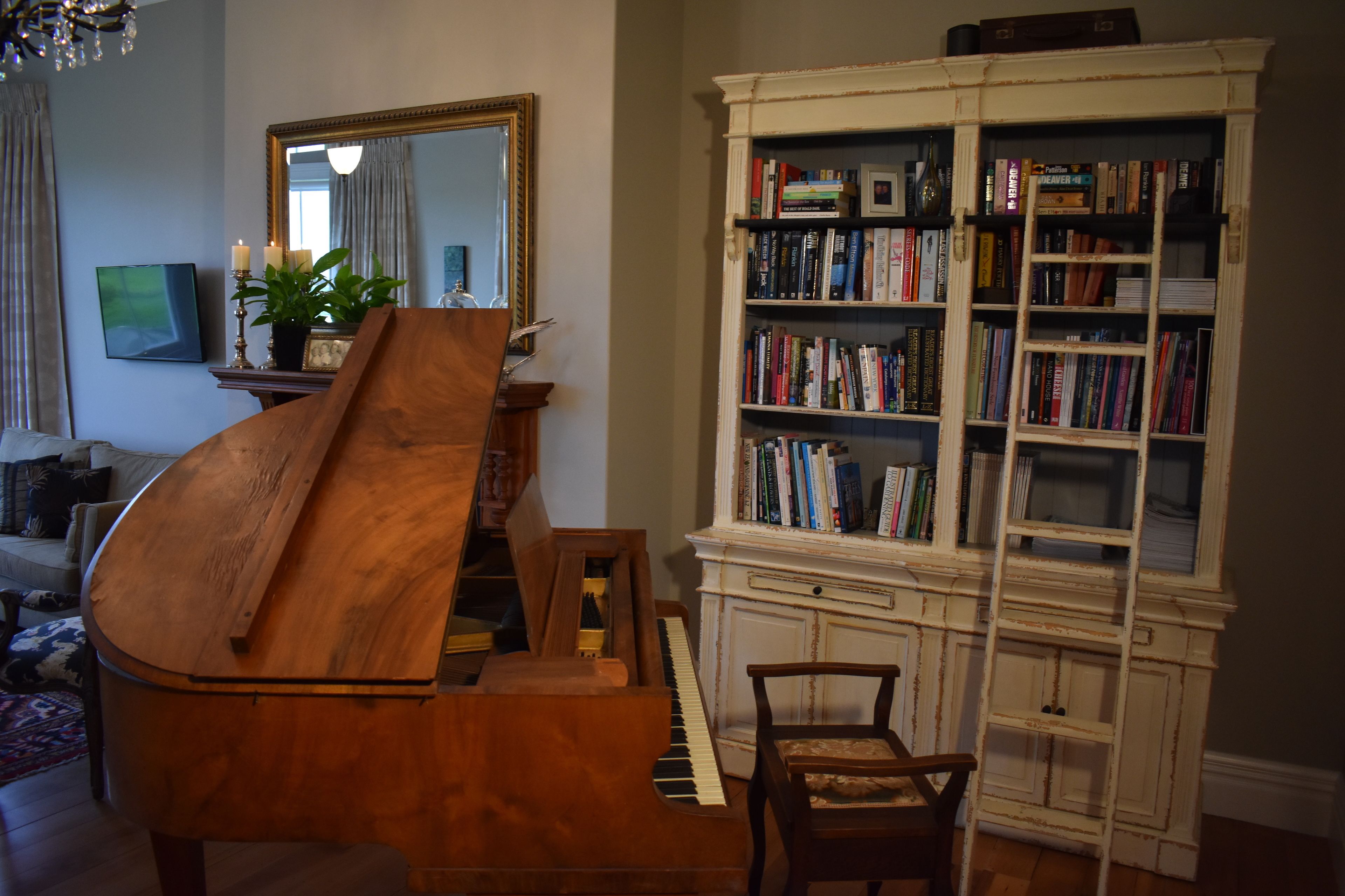 Un piano de cola en una sala de estar con una estantería y un espejo.
