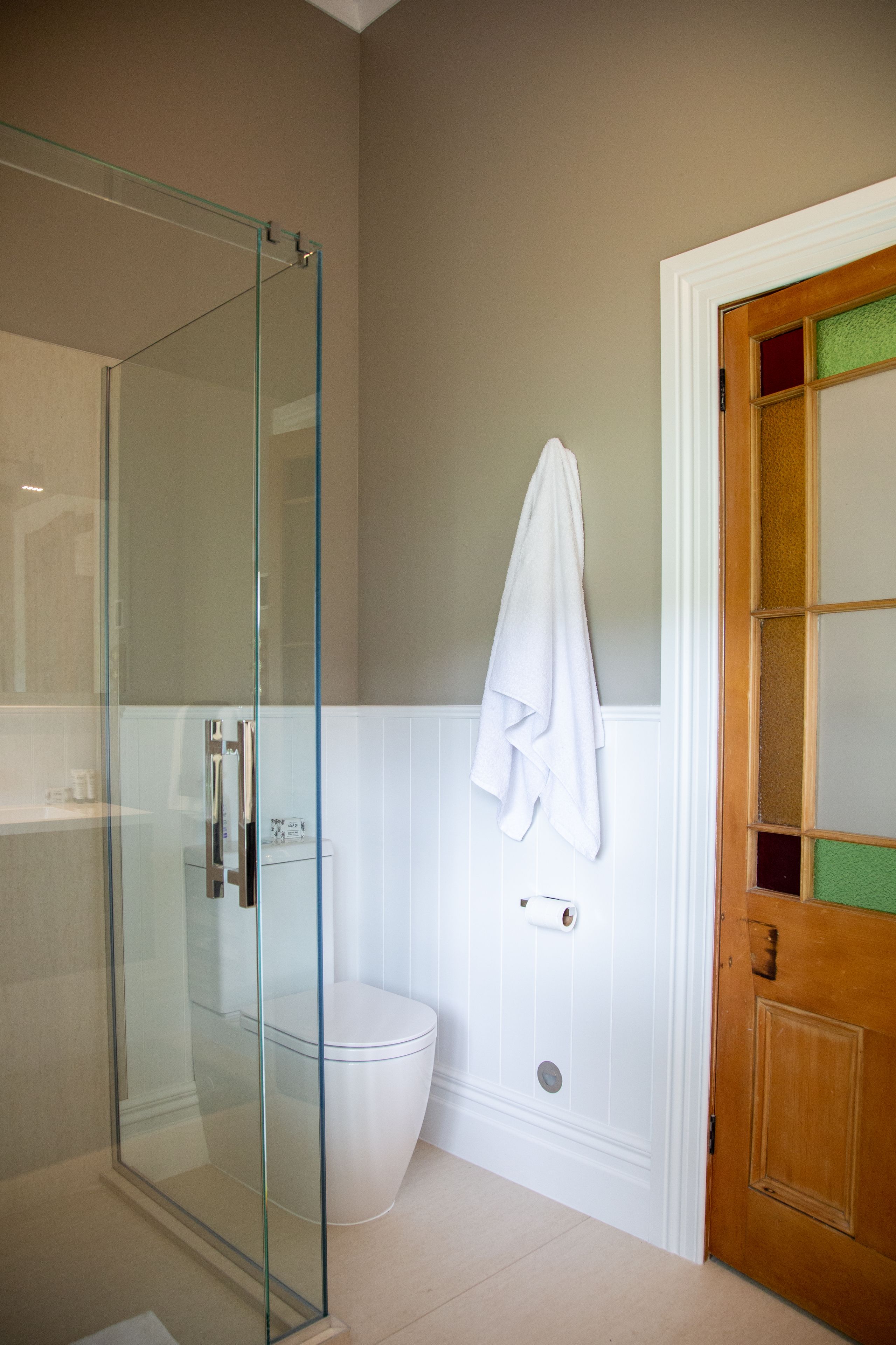 A bathroom with a glass shower enclosure, a white toilet, and a wooden door with a glass panel.