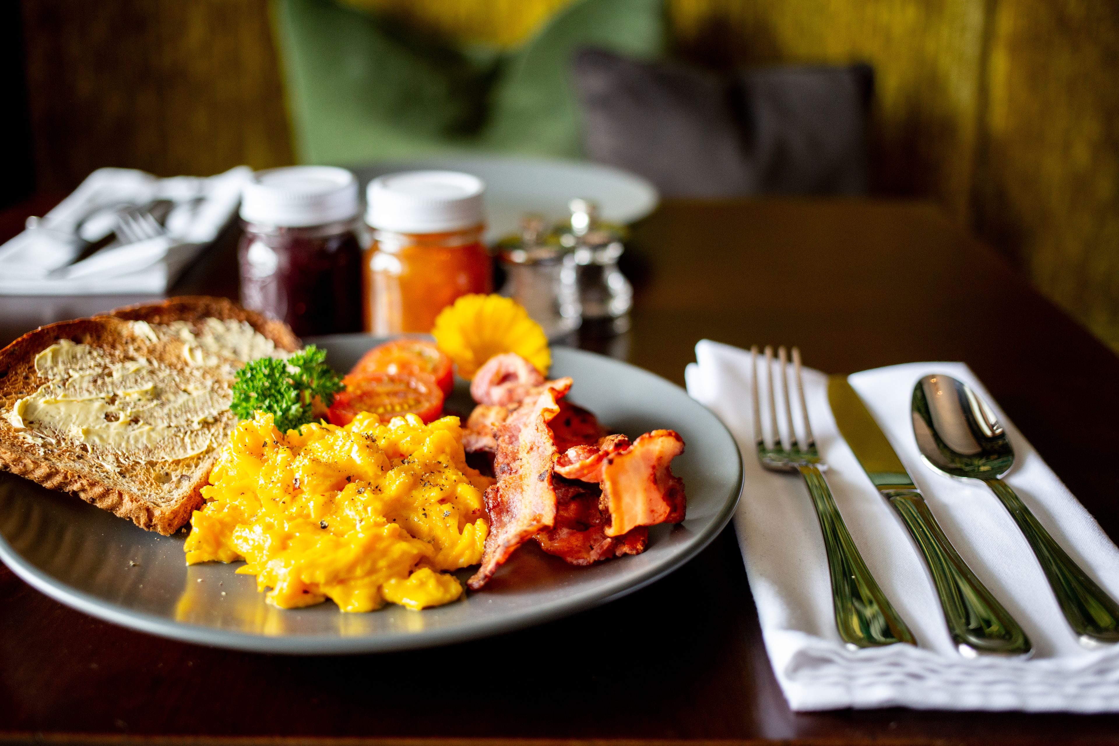 Une assiette de petit-déjeuner avec des toasts, des œufs brouillés, du bacon et une garniture, posée sur une table avec une serviette et des couverts.