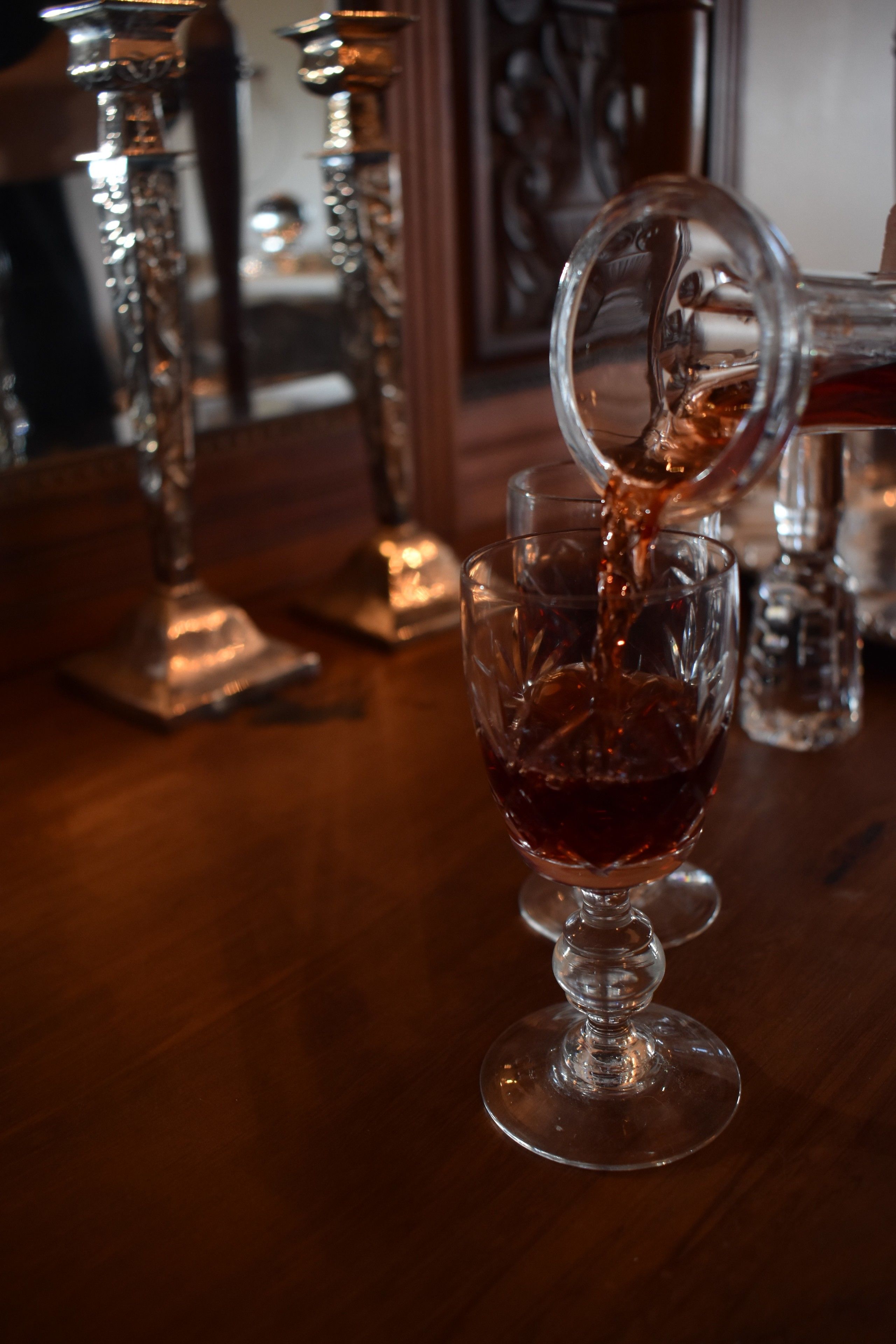Een glas rode vloeistof wordt in een ander glas gegoten op een houten tafel.