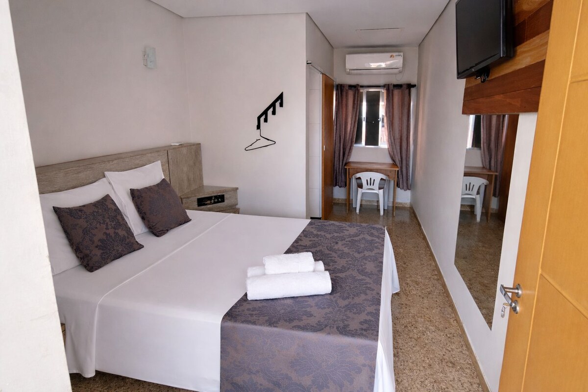 A hotel room with a bed, bedside table, and a TV mounted on the wall.
