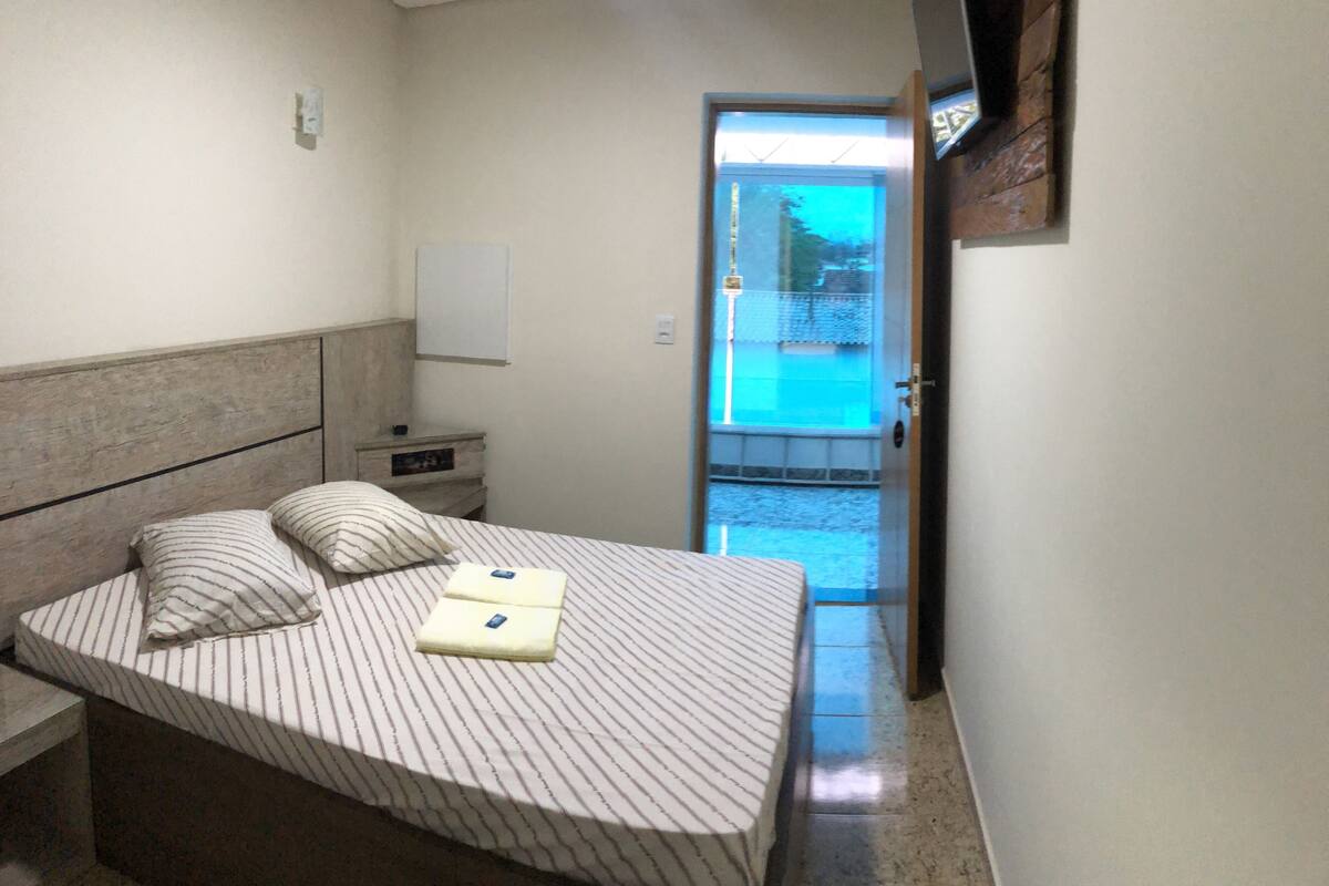 A bedroom with a bed, a nightstand, a wall-mounted TV, and a door leading to a balcony.