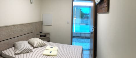 Un dormitorio con cama, una mesita de noche, un televisor de pared y una puerta que da a un balcón.