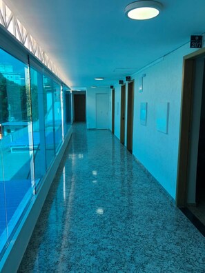 A long, narrow hallway with glass walls on one side and doors on the other, leading to individual rooms. - Hotel Butantã (São Paulo)