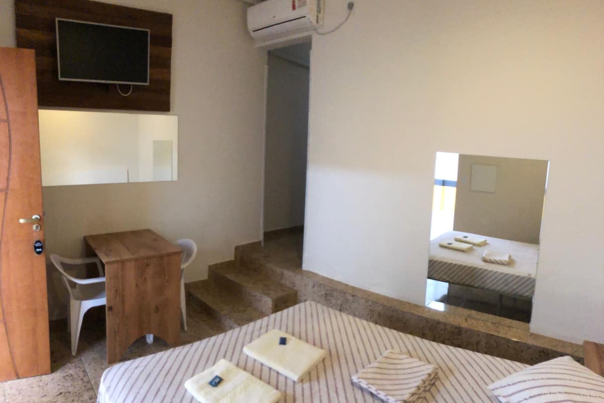 A bedroom with a bed, a desk, a chair, a TV mounted on the wall, and a mirror.