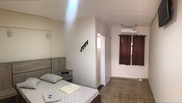 Una habitación de hotel con una cama, mesita de noche y televisor montado en la pared.
