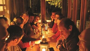 A group of people seated around a wooden table with candles and wine glasses, suggesting a social gathering or dinner setting. - Peter's Farm Lodge (Waipiata)
