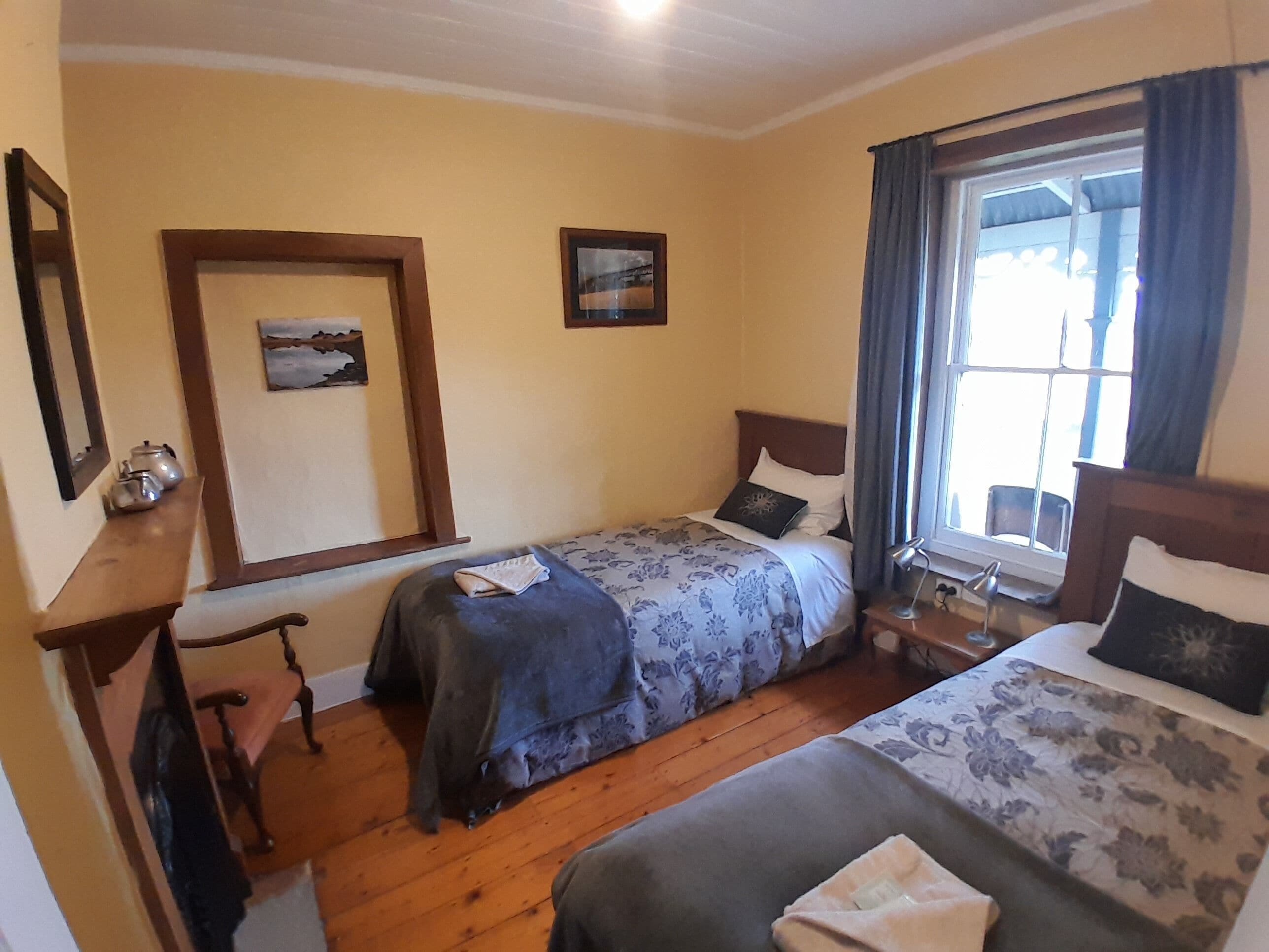 A hotel room with two beds, wooden flooring, a desk, a chair, and a window with curtains.