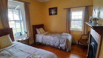 A bedroom with two beds, a small table, a chair, and a window with curtains.