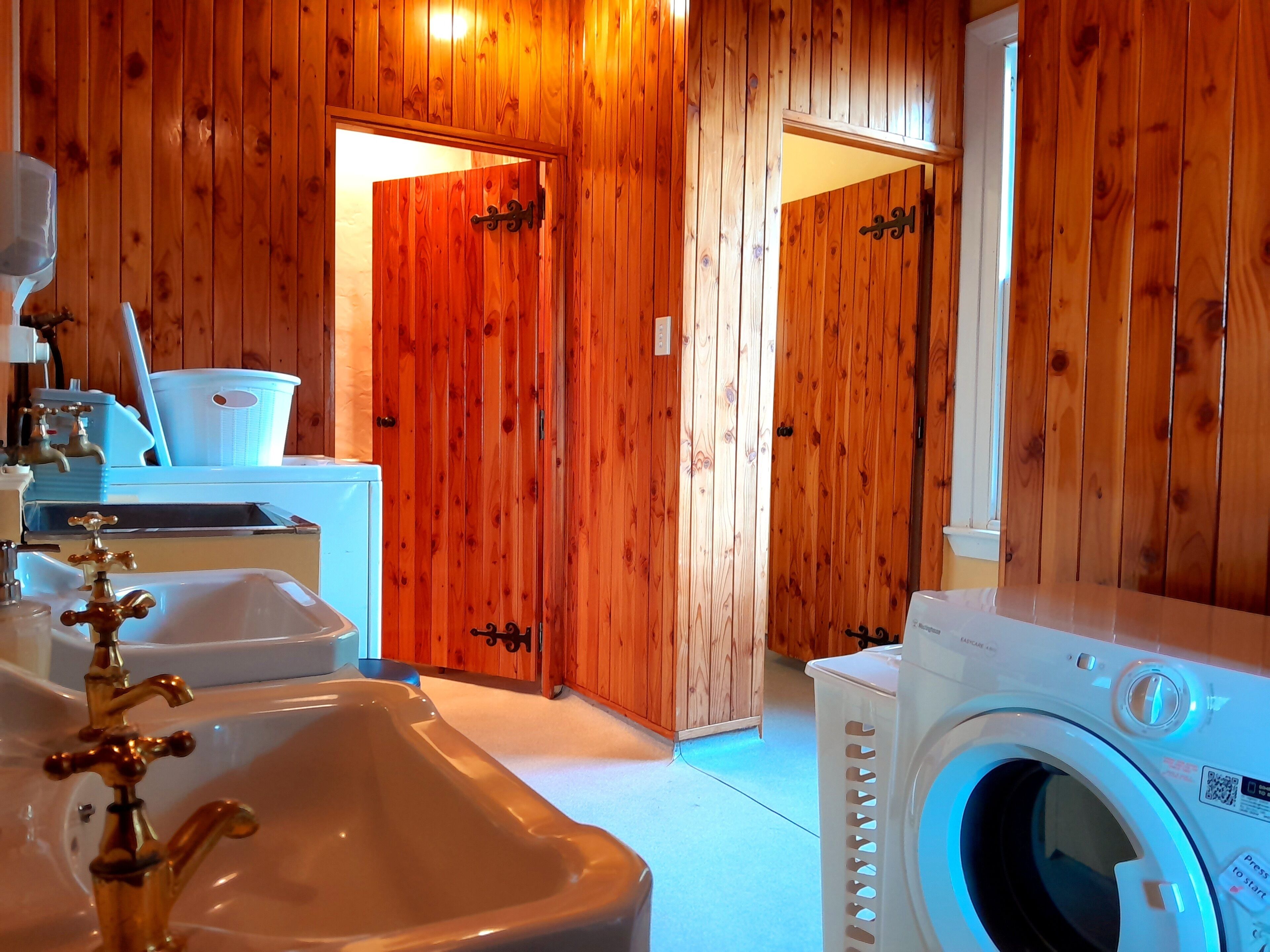 Quarto com paredes de madeira, pia com torneira dourada, máquina de lavar e porta que dá para outro espaço.