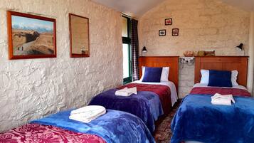 A room with two beds, each with a blue and red bedspread, a wooden headboard, and a painting of a mountainous landscape on the wall.