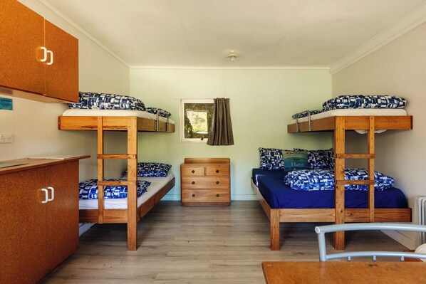 Une chambre de dortoir avec des lits superposés, une commode en bois, une petite table et une fenêtre avec des rideaux.