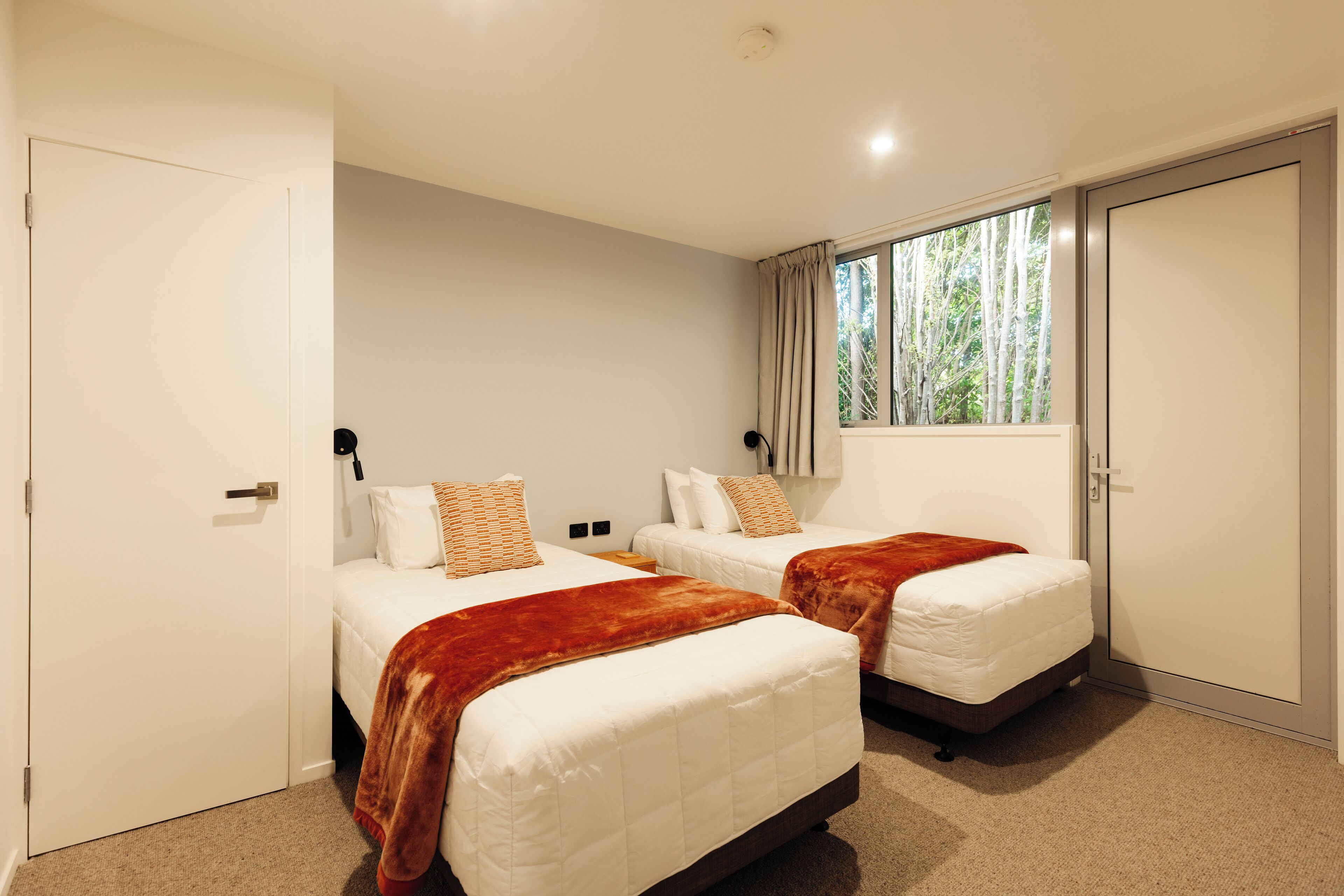 Habitación de hotel con dos camas, una ventana con cortinas y una puerta.