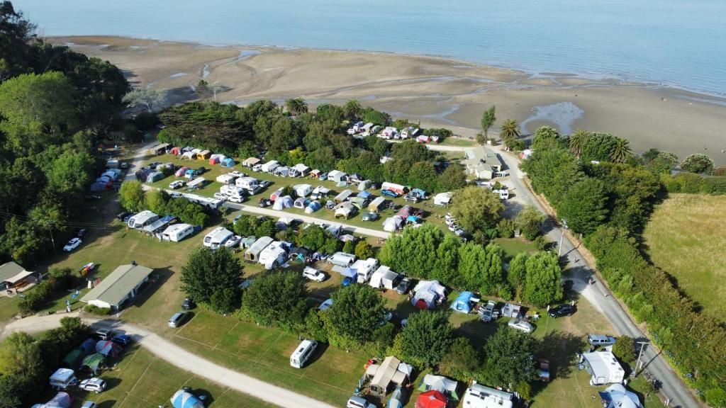 Luchtbeeld van een camping met campers en tenten, omgeven door bomen en een strand.