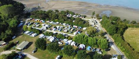 Luchtbeeld van een camping met campers en tenten, omgeven door bomen en een strand.