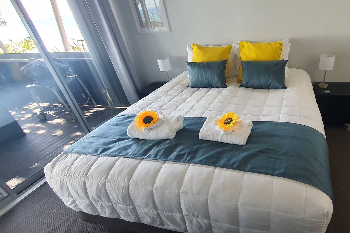 A hotel room with a large bed, two nightstands, a window with a view, and a door leading to a balcony.