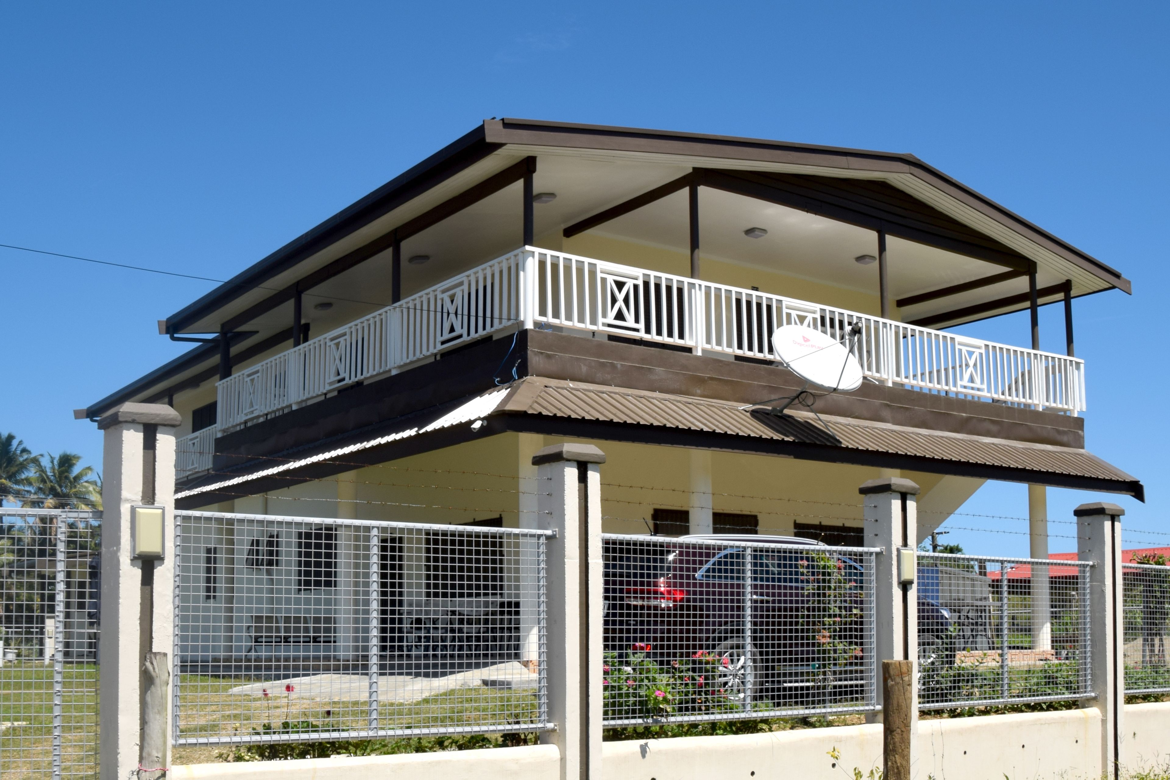 A two-story building with a balcony, surrounded by a metal fence.