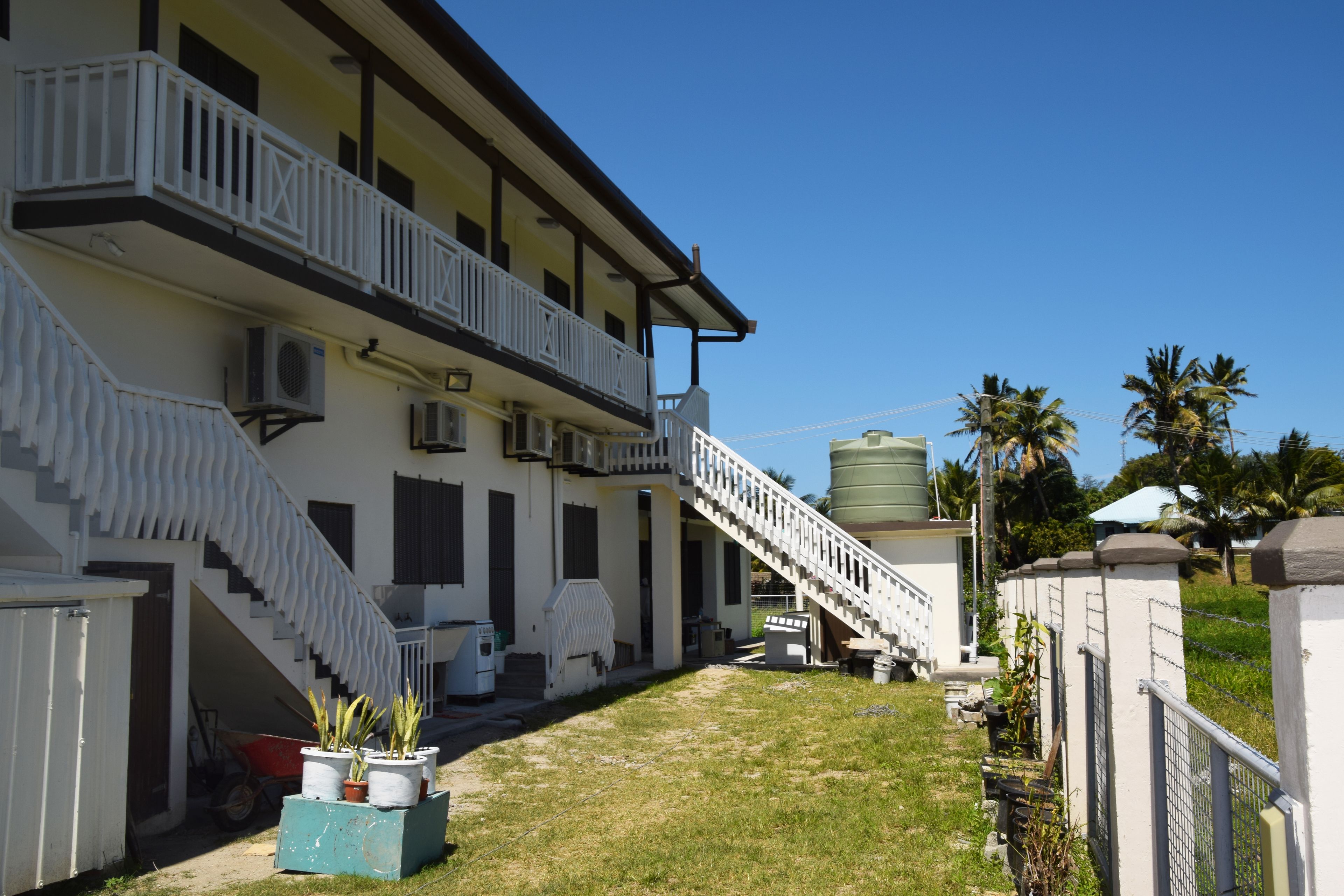 Un edificio de dos pisos con balcón, escalera y depósito de agua.