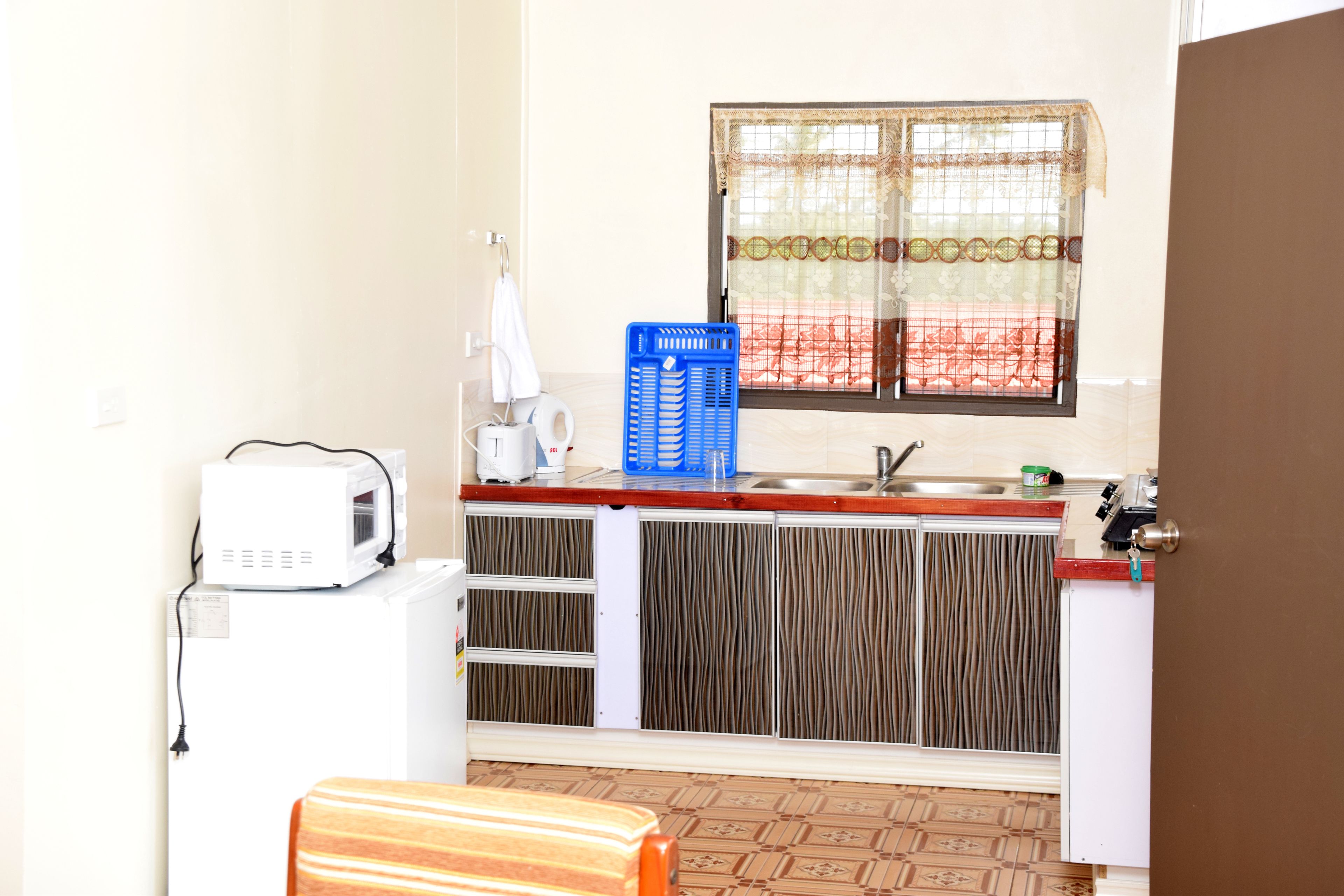 Una cocina compacta con microondas, un lavabo y una ventana con cortina decorada.