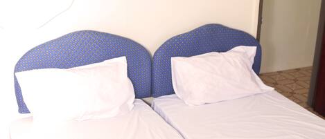 A single bed with a white mattress and blue headboard, a white pillow, and a white blanket.