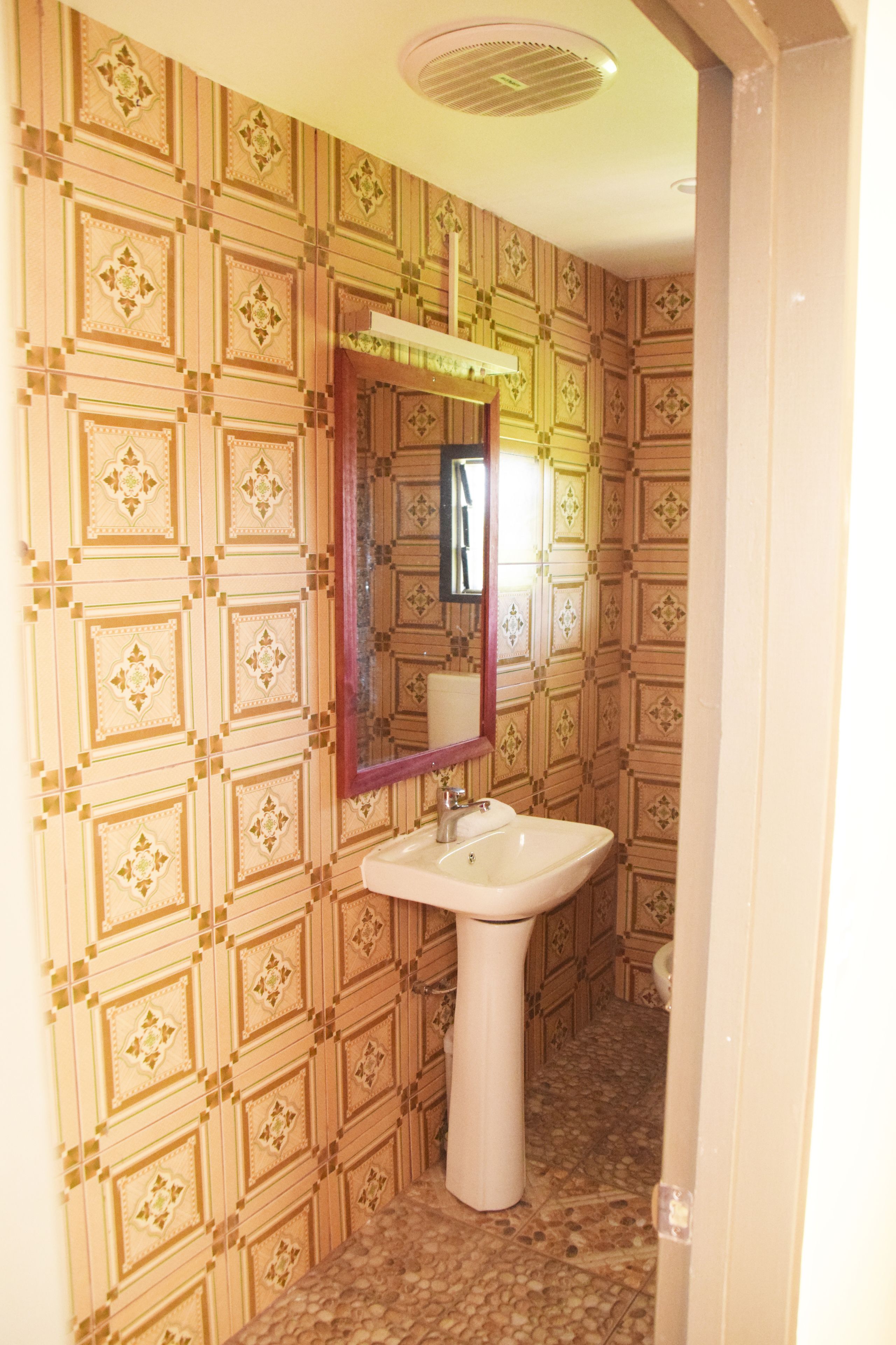 A bathroom with patterned wallpaper, a pedestal sink, and a mirror with a wooden frame.