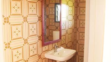 A bathroom with patterned wallpaper, a pedestal sink, and a mirror with a wooden frame.