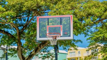 A basketball hoop with a red and white frame, surrounded by lush green trees.