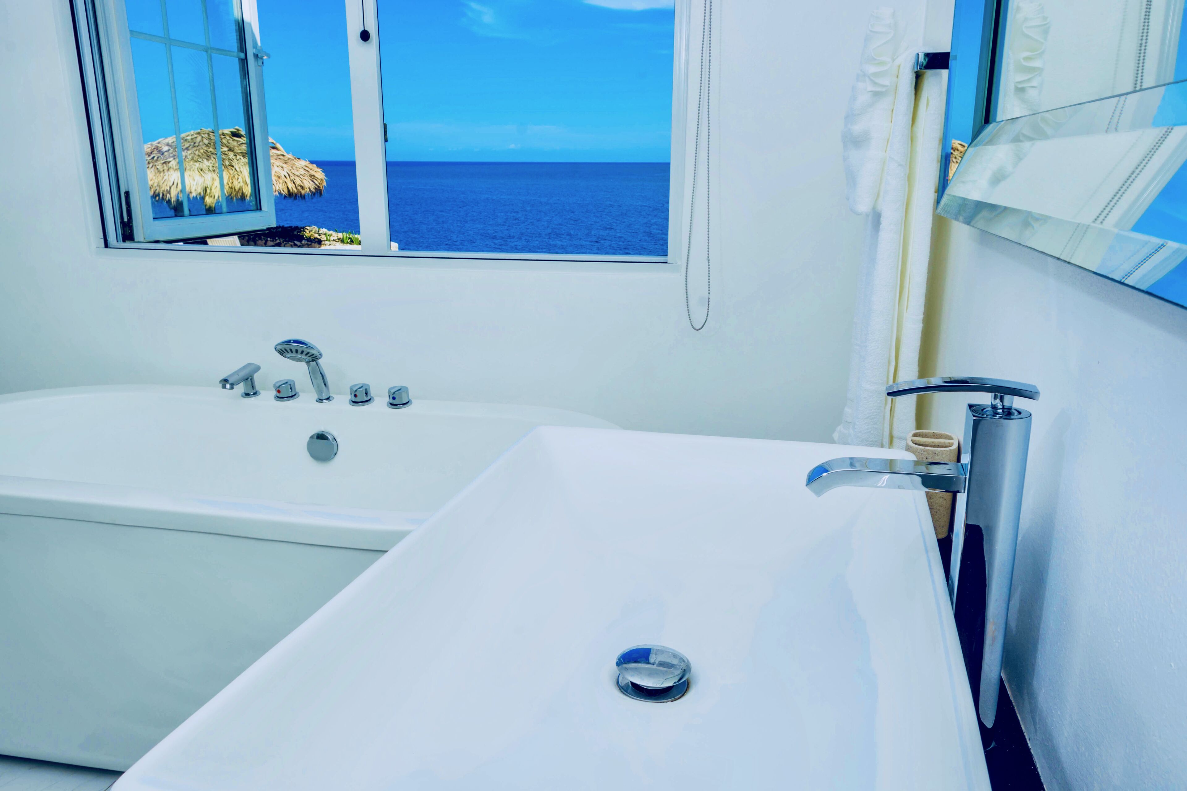 Une salle de bain moderne équipée d’une baignoire, d’un lavabo et d’une grande fenêtre donnant sur la mer.
