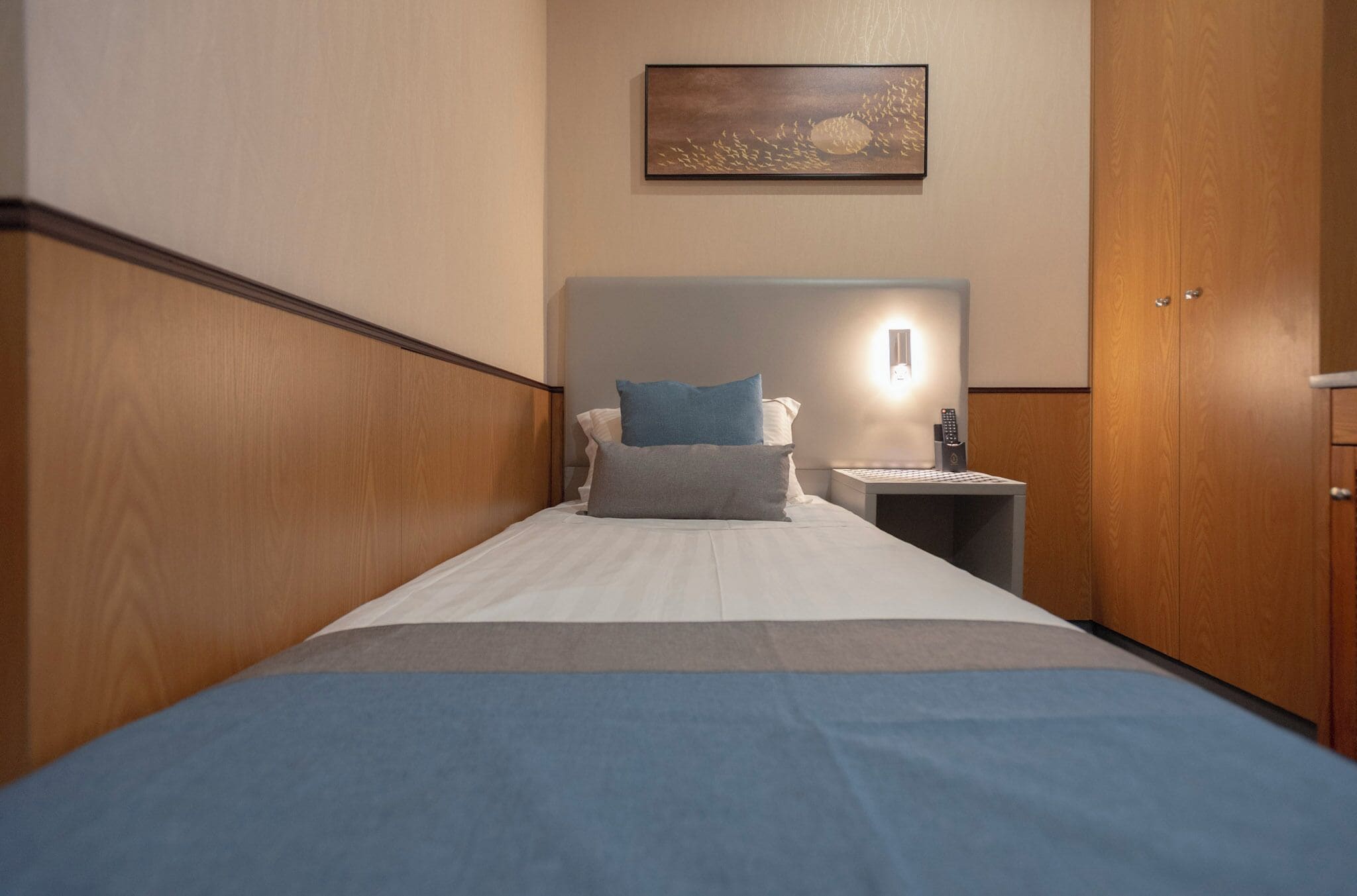 Een hotelkamer met een bed, een nachtkastje, een wandlamp en een houten garderobe.