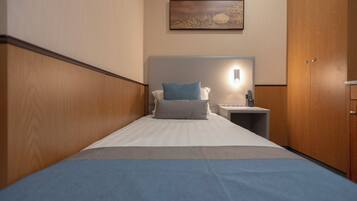 A hotel room with a bed, a nightstand, a wall-mounted light, and a wooden wardrobe.