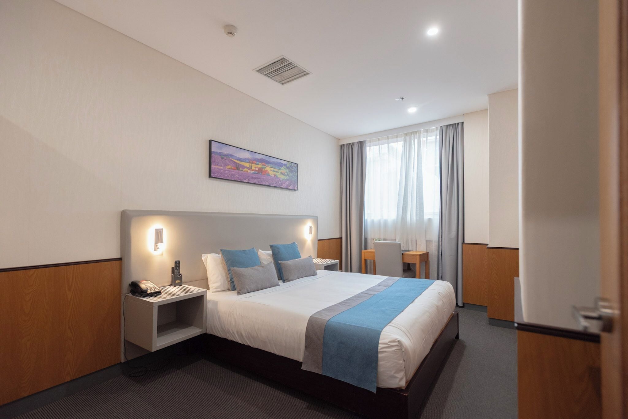 A hotel room with a large bed, bedside tables, a desk, and a chair.