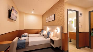 A hotel room with two beds, a TV mounted on the wall, and a bathroom visible through an open door.