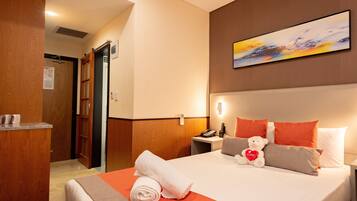 A hotel room with a bed, a desk, a chair, a painting on the wall, and a door.