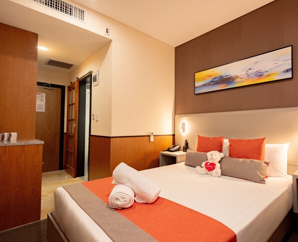 A hotel room with a bed, a desk, a chair, a painting on the wall, and a door.