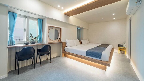 A modern bedroom with a bed, desk, chairs, and a window with curtains. - Jeongdongjin Motel (Gangneung)