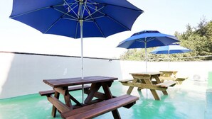 A patio area with picnic tables and blue umbrellas. - Jeongdongjin Motel (Gangneung)