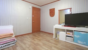 A room with striped wallpaper, a wooden door, a television on a white stand, and a stack of folded blankets. - Jeongdongjin Motel (Gangneung)