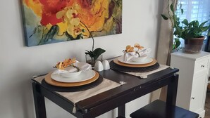 A dining table with two white plates and yellow napkins, a potted plant, and a painting of flowers on the wall.