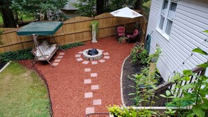 A backyard with a fire pit, a wooden fence, and a patio area with chairs and an umbrella.